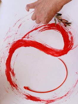 Eine Malschülerin malt gestisch mit roter Farbe. Als Pinsel dient ihr ein Ölzweigchen.